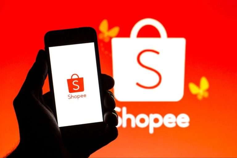 Logo Shopee terlihat di layar ponsel dengan latar belakang merah dan logo Shopee yang lebih besar.